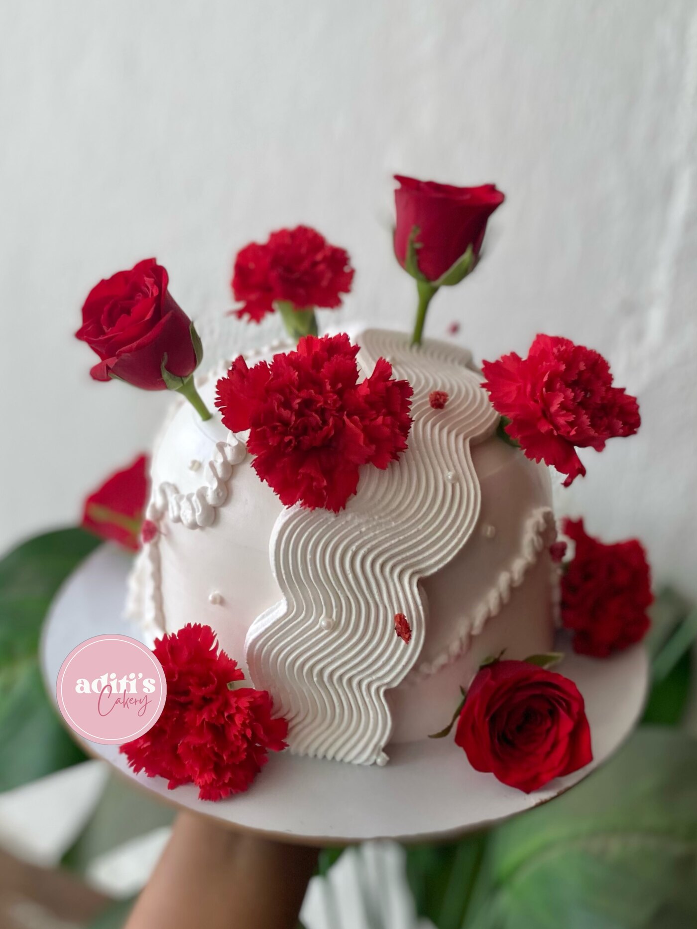White celebration cake crowned with fresh red roses by Aditi's Cakery